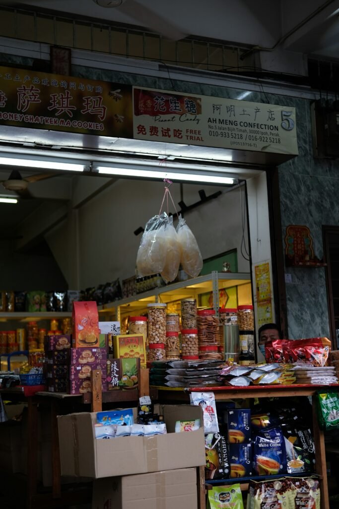 A well-organized retail shop in Nigeria with shelves fully stocked with provisions, including tin tomatoes, milk, soap, and cereal. The shop owner stands attentively nearby.