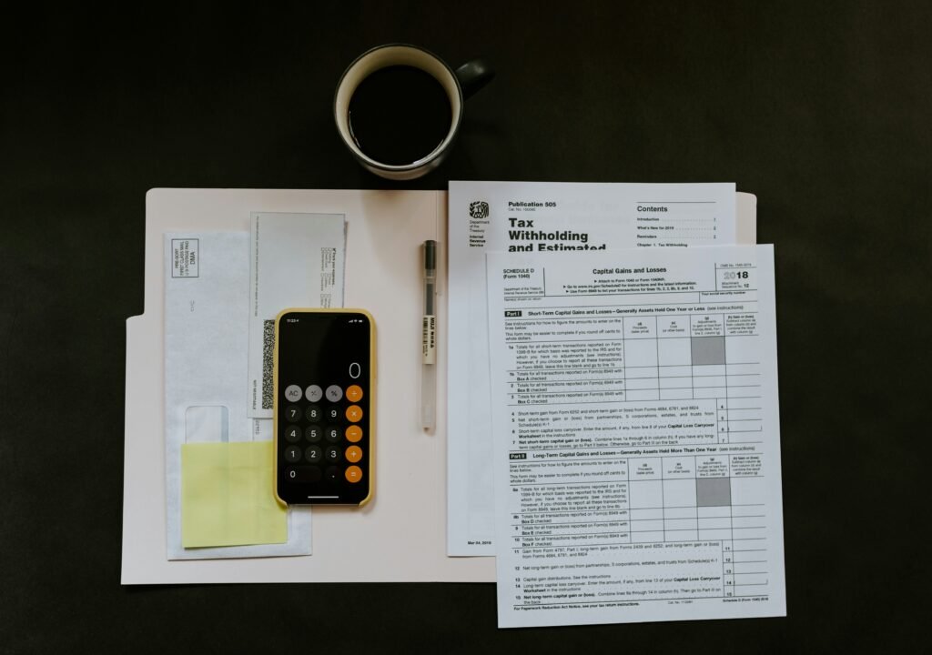 An overhead view of a small business accounting setup: scattered papers with handwritten numbers, a simple calculator, a biro pen, and a cup of coffee.