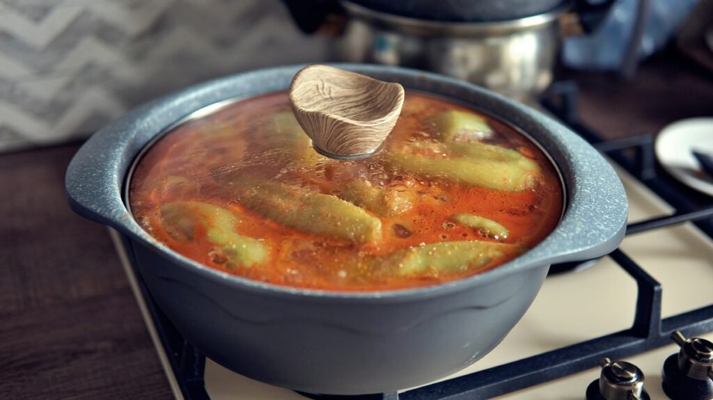 A large, steaming pot of rich Nigerian stew simmering over a fire, with a ladle resting against its side.