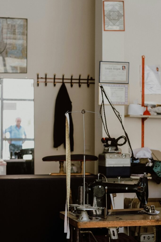 A close-up of a tailor's sewing machine in a Nigerian workshop, with spools of colorful thread and Ankara fabric nearby.