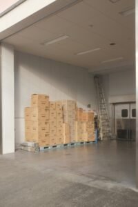 A dimly lit warehouse interior filled with stacked cardboard boxes of various sizes, representing the physical reality behind dropshipping operations.